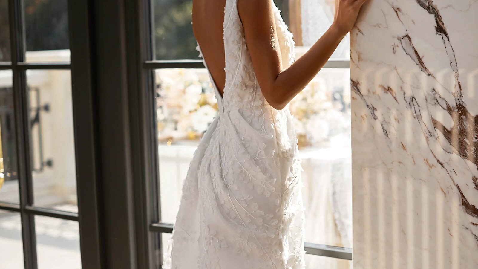 Textured white wedding dress beside sunlit atelier windows.